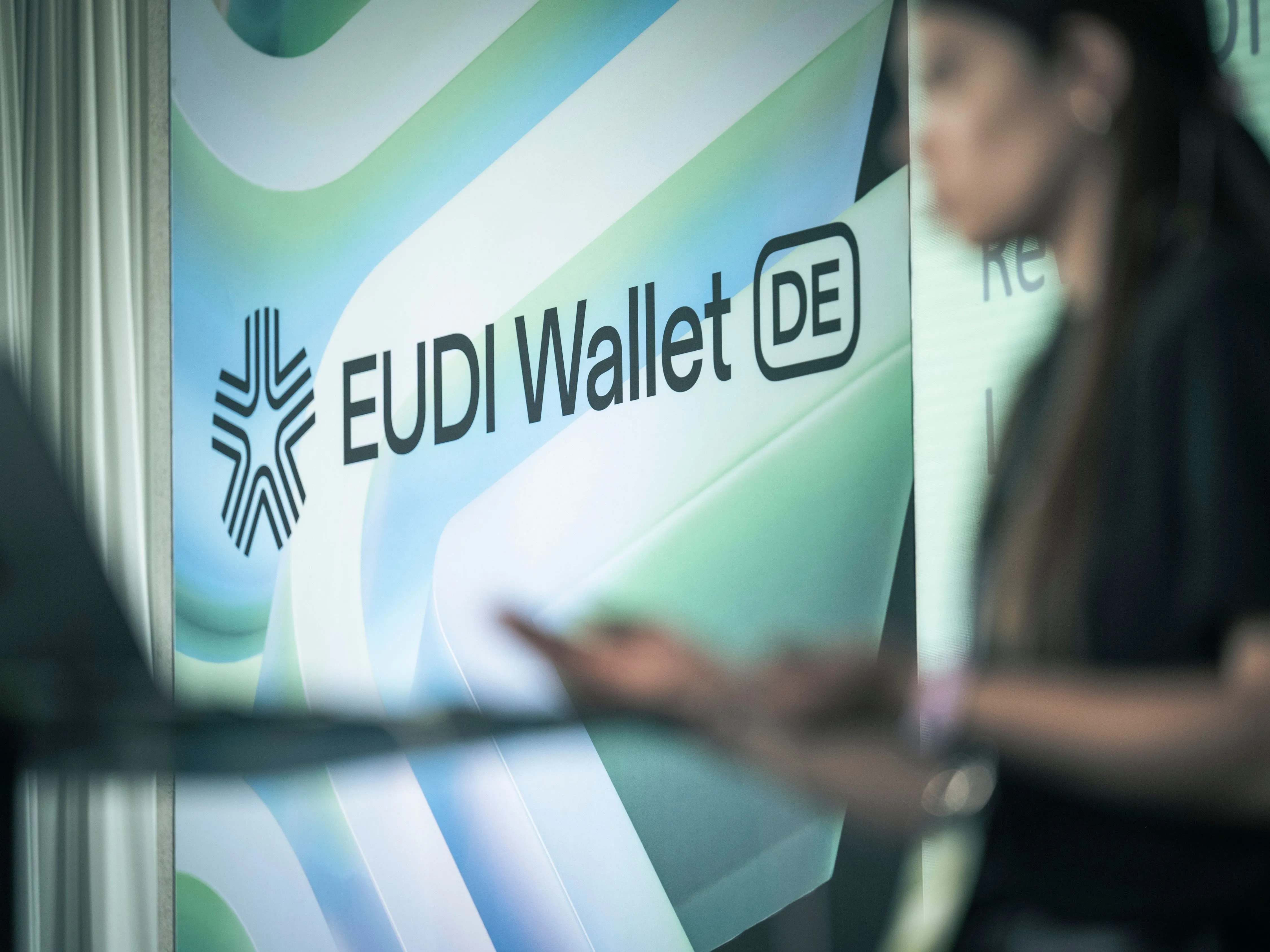 Close-up of an EUDI Wallet logo on an information panel, with a blurred person in the foreground