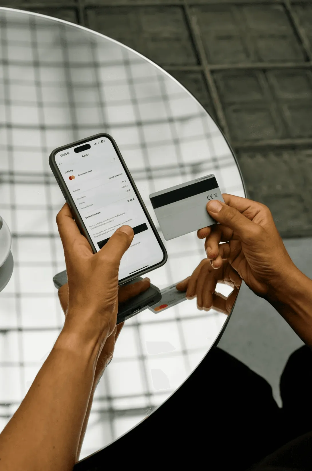 Picture of a person making an online payment, holding a smartphone that displays a checkout page and a credit card