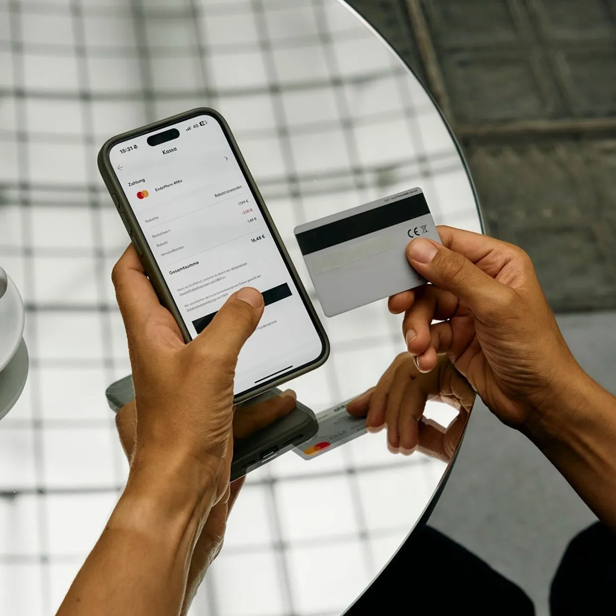 Bild einer Person, die eine Online-Zahlung durchführt. Sie hält ein Smartphone mit einer geöffneten Bezahlseite und eine Kreditkarte in den Händen.