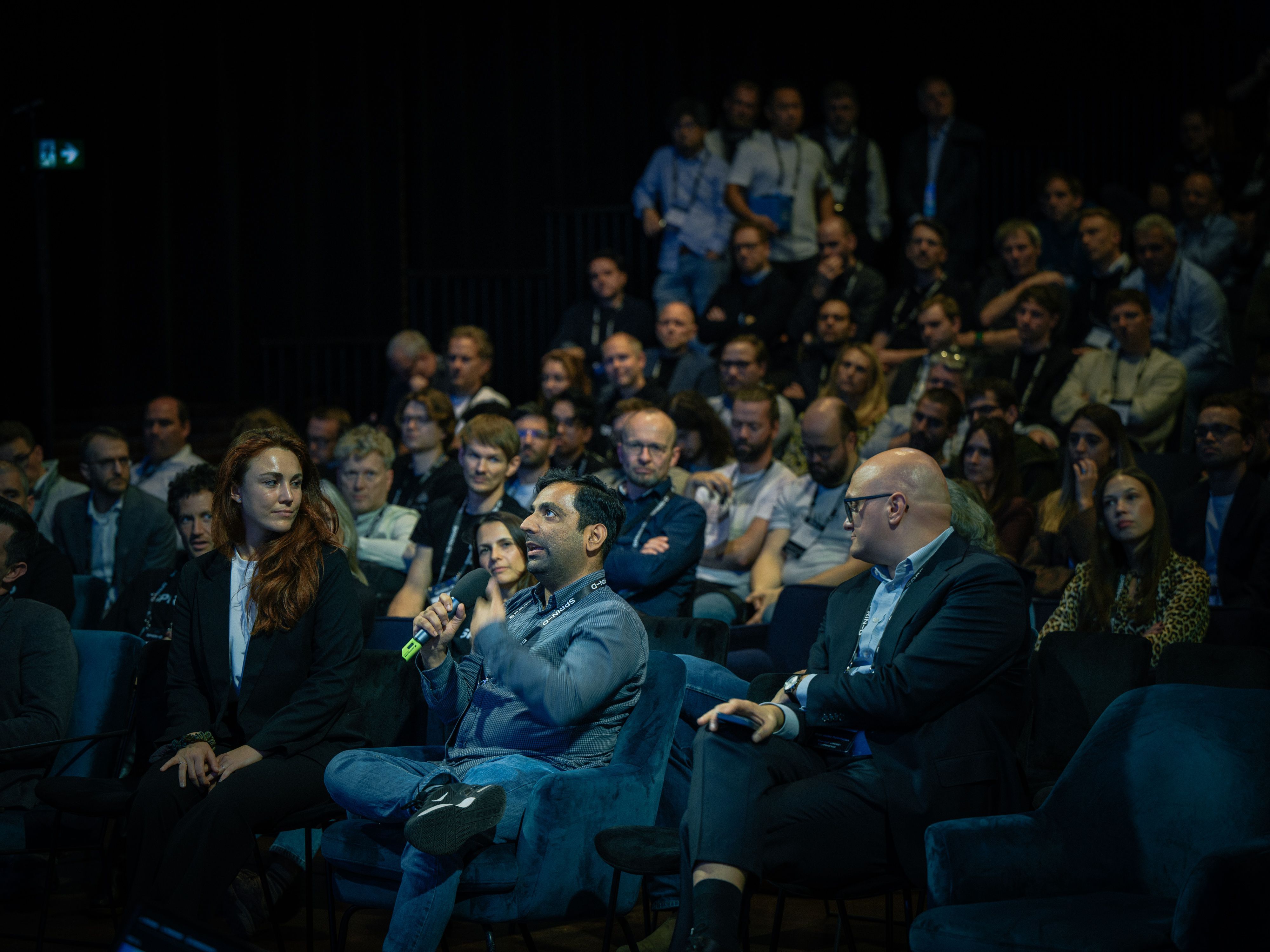 Picture of an audience sitting in a dark room, attentively watching a presentation