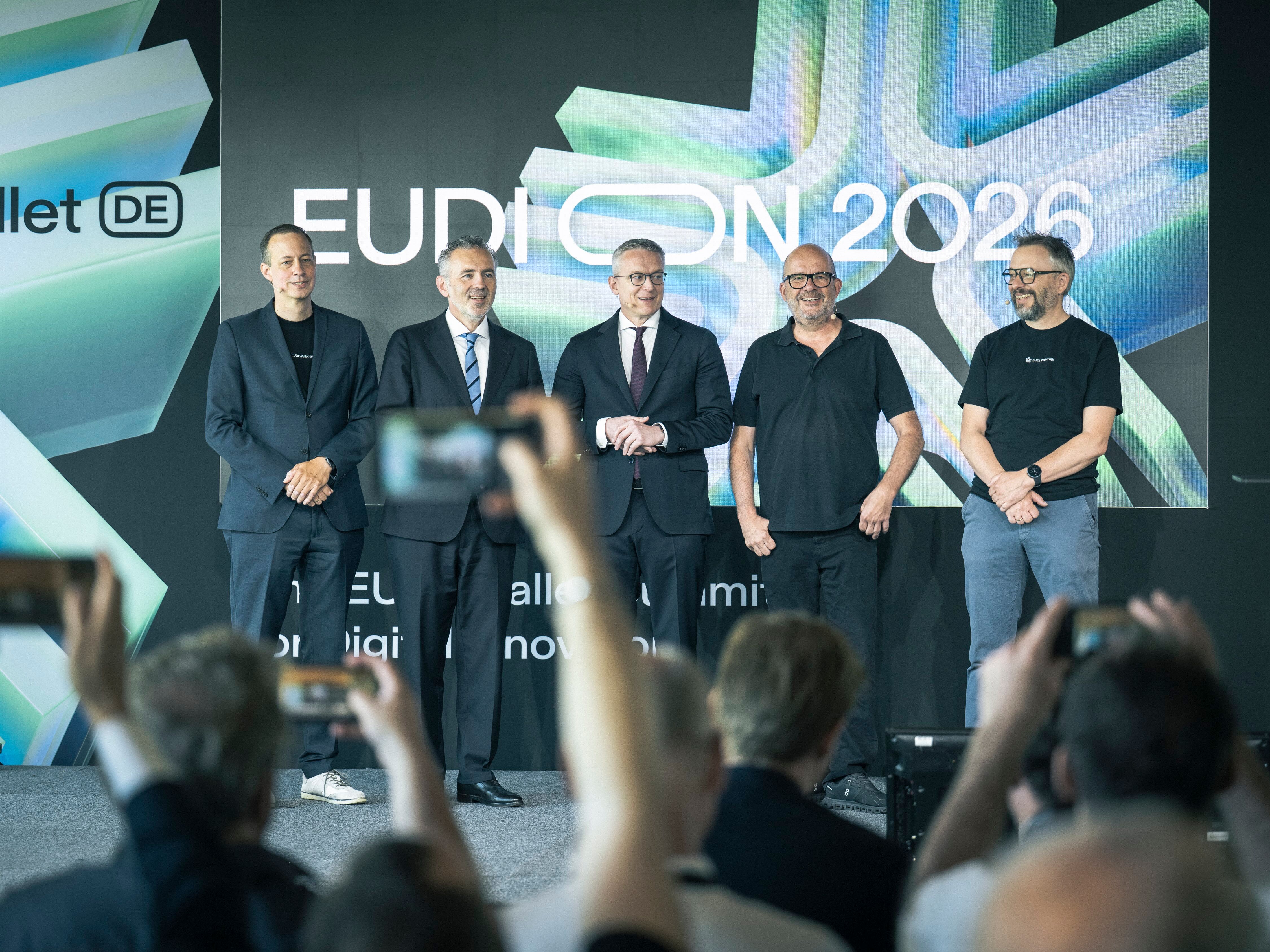 Mehrere Personen stehen auf einer Bühne vor einer großen EUDION‑2026‑Projektionsfläche, während das Publikum davor Fotos macht