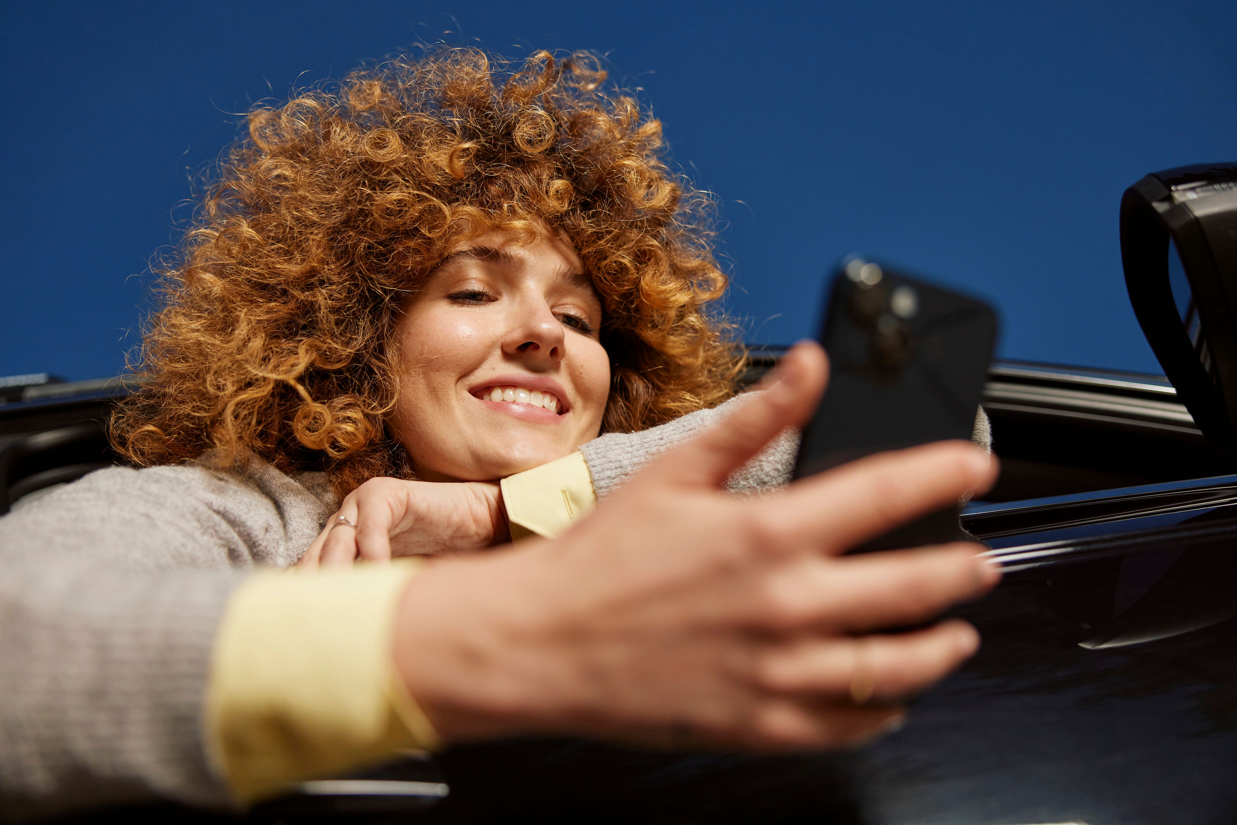 girl with curly hair, leaning out of car window, smiling at phone