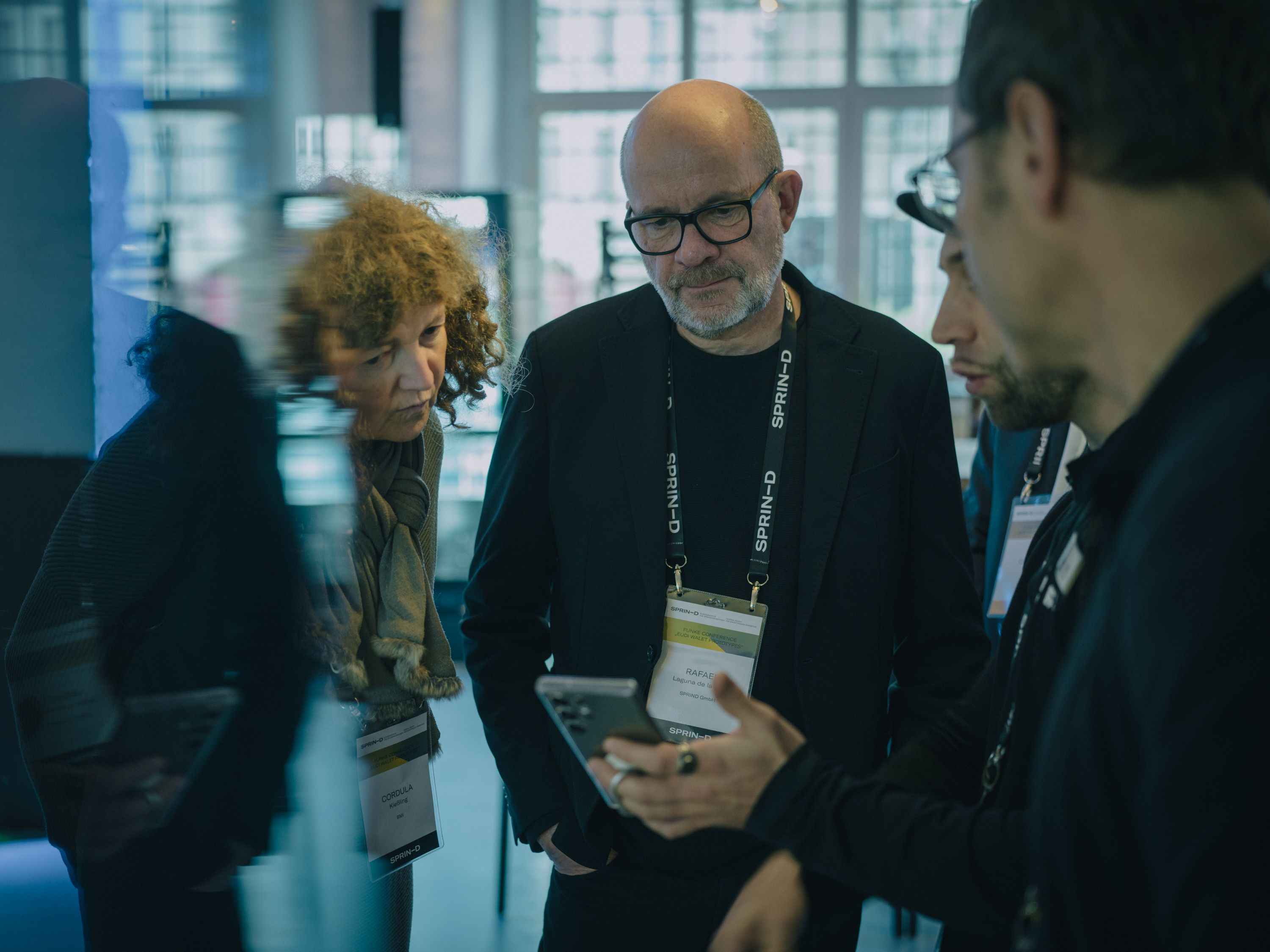 Gesprächssituation an einem Messestand zur EUDI‑Wallet, bei der mehrere Personen Informationen austauschen vor einem Bildschirm mit Projektinformationen