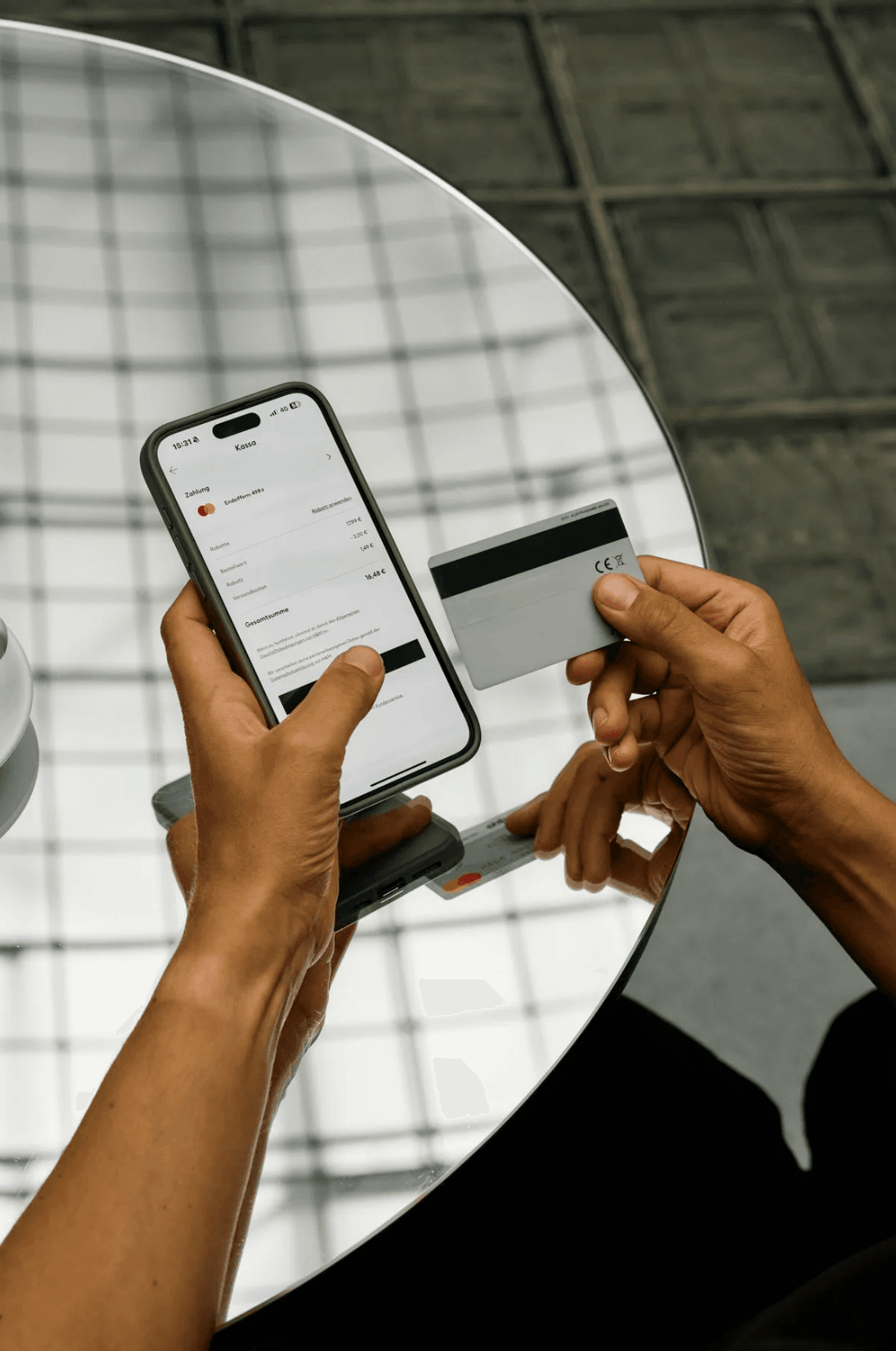 Picture of a person making an online payment, holding a smartphone that displays a checkout page and a credit card